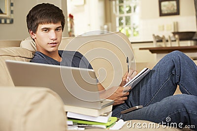 Teenage Boy Sitting On Sofa At Home Doing Homework Using Laptop Computer Stock Photo