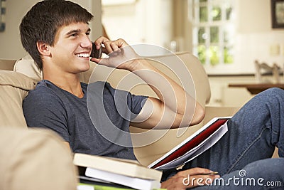 Teenage Boy Sitting On Sofa At Home Doing Homework Using Mobile Phone Stock Photo