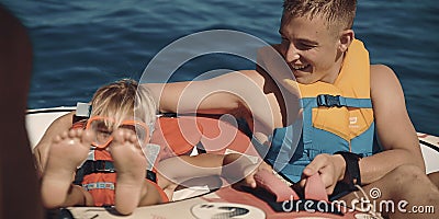 Teenage boy with young boy on holiday sitting on inflatable rib wearing life jackets in the ocean Editorial Stock Photo