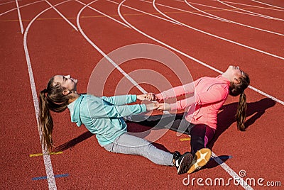 Teenage friends do partner stretch exercises on athletics track, friendship Stock Photo