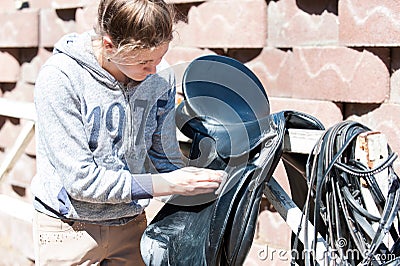 Teenage girl equestrian cleans black Leather Horse Saddle Stock Photo