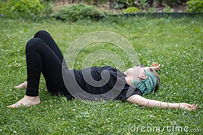 A teenage girl in glasses with multi-colored hair is tired of games and lies on the lawn in a summer garden Stock Photo