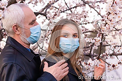 Teenage girl and grandfather in face mask. Standing in a flowering garden, support during pandemic, .senior man worry about gra Stock Photo