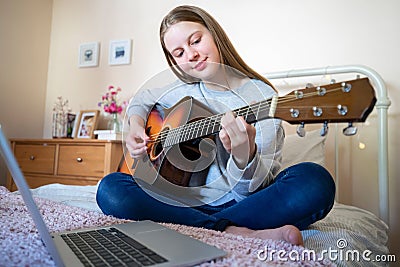 Teenage Girl Learning To Play Acoustic Guitar With Online Lesson On Laptop Computer Stock Photo