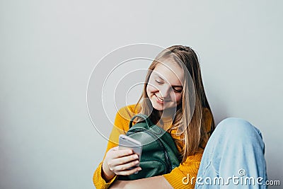 Teenage girl looking on cellphone and smiles chatting with friends. Beautiful girl in yellow sweater and blue jeans holding mobile Stock Photo