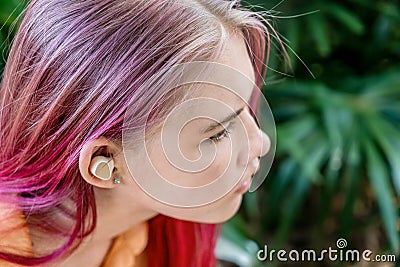 Teenage girl with ombre colored pink hair with wireless earbuds earphones. Music phone calls podcast audiobooks listening Stock Photo