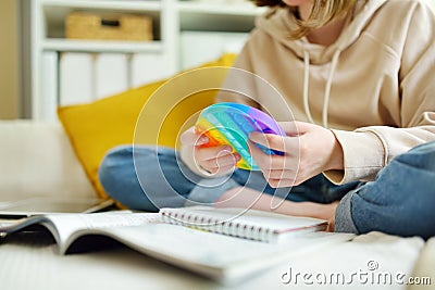 Teenage girl playing with rainbow pop-it fidget toy while studying at home. Teen kid with trendy stress and anxiety relief Stock Photo