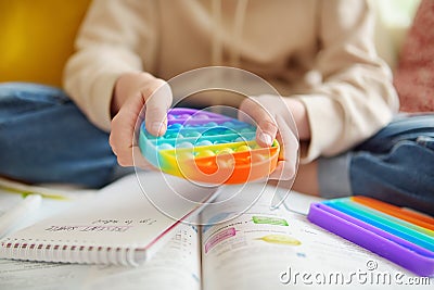 Teenage girl playing with rainbow pop-it fidget toy while studying at home. Teen kid with trendy stress and anxiety relief Stock Photo