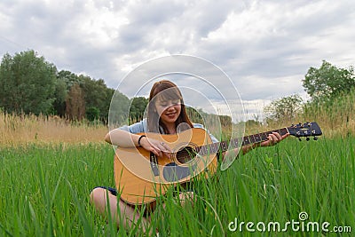 Teenage girl portrait photography with acoustic guitar model posing outdoor green field peaceful summer June day time nature Stock Photo