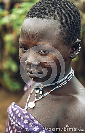 TOPOSA TRIBE, SOUTH SUDAN - MARCH 12, 2020: Teenage girl with scarred face and traditional accessories looking away while living Editorial Stock Photo