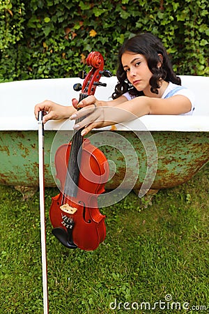 Teenage girl holding violin and fiddlestick outdoor in bathtub Stock Photo