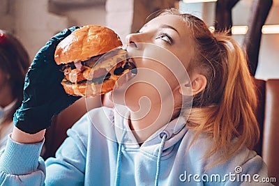 Teenage girl sitting in cafe, eating burger Stock Photo