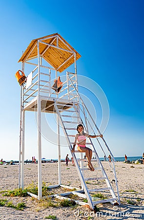 Teenage girl sitting on stairs lifeguard tower on beach against cloudless sky Stock Photo