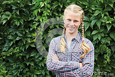 A teenage girl is smiling in the summer garden against a background of a wall of green leaves. Stock Photo