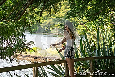 Teenage girl in shade stands by railing looking at lake Stock Photo