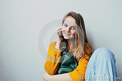 Teenage girl talking on a cellphone and smiles looking at camera. Beautiful girl in yellow sweater and blue jeans holding mobile p Stock Photo