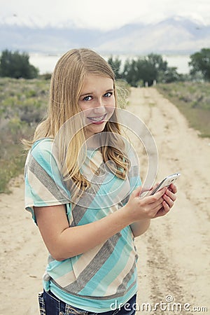 Teenage girl using cellphone walking down a country dirt road Stock Photo