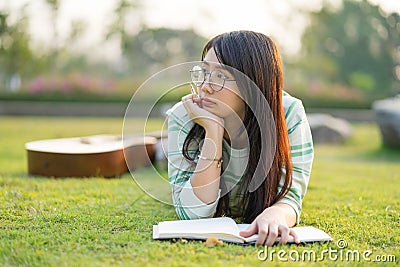 Teenage girl wearing glasses lying down with guitar and books On the field at sunset. Stock Photo
