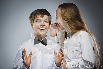 Teenage girl whispering in the ear of teen boys on a gray background. Positive human emotion, facial expression. Closeup Stock Photo