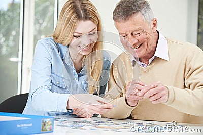 Teenage Granddaughter Helping Grandfather With Jigsaw Puzzle Stock Photo