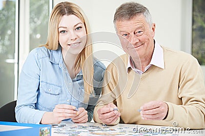 Teenage Granddaughter Helping Grandfather With Jigsaw Puzzle Stock Photo