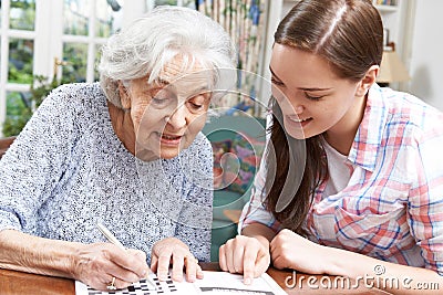 Teenage Granddaughter Helping Grandmother With Crossword Puzzle Stock Photo