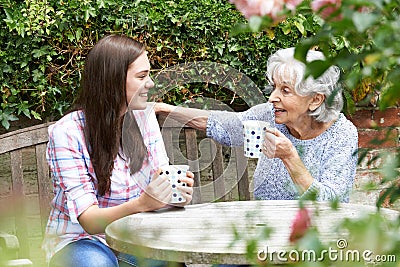 Teenage Granddaughter Relaxing With Grandmother In Garden Stock Photo