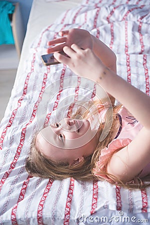 Teenage lying on her back bed and looks in phone Stock Photo