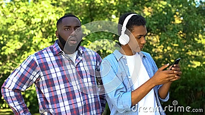 Teenage male in earphones with smartphone ignoring displeased father puberty age Stock Photo