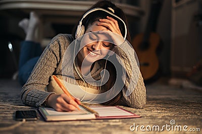 Schoolgirl at home doing her homework while listening to music with headphones Stock Photo