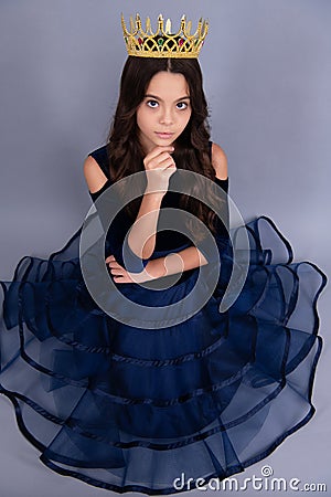 Teenage selfish girl in ball dress celebrates success victory. Teen child in queen crown on grey background Stock Photo