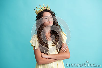 Teenage selfish girl celebrates success victory. Teen child in queen crown isolated on blue background. Princess girl in Stock Photo