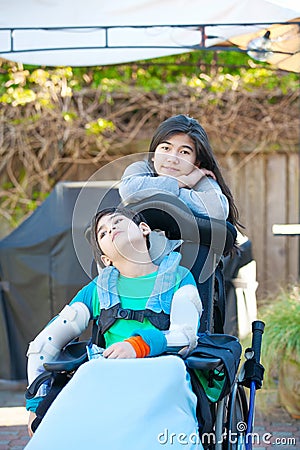 Teenage sister taking care of disabled brother in wheelchair out Stock Photo