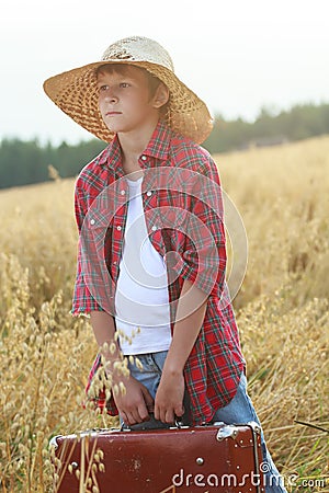 Teenage traveler in farm oat field holding old-fashioned suitcase and looking to horizon Stock Photo