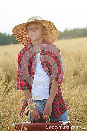 Teenage traveler in farm ripe oat field with old-fashioned brown suitcase looking at camera Stock Photo