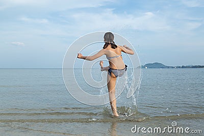 Teenage wearing bikini kicks the sea water at the beach. Stock Photo