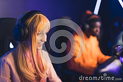 Teenage white girl wearing headset smiling competing in online game tournament with her friend. Blurred background. Blue Stock Photo