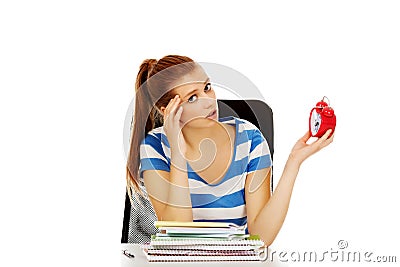 Teenage woman sitting behind the desk and holding alarm clock Stock Photo