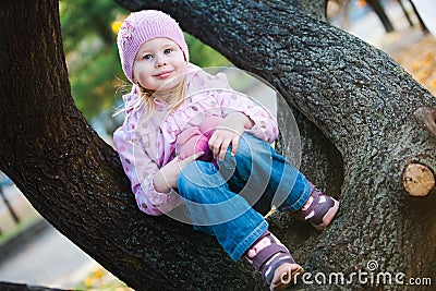 Teenaged girl sitting with teddy bear on tree - purple dots jacket. Stock Photo