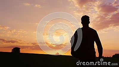 A teenager with a backpack over his shoulder goes towards the sunset in the field or in the countryside. Concept - new Stock Photo