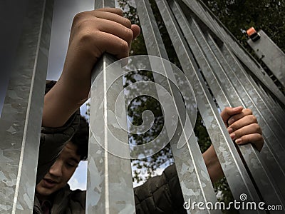 Teenager boy hands holding strong iron bars. Seen from below. Immigrant and refugee crisis. Dramatic border fence or prison concep Stock Photo