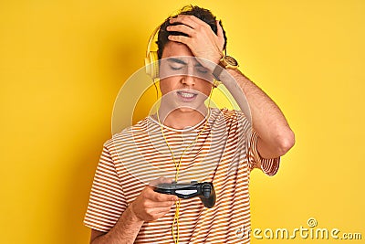 Teenager boy playing video games using gamepad over isolated yellow background stressed with hand on head, shocked with shame and Stock Photo