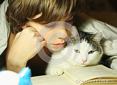 Teenager boy reading book with cat in bed Stock Photo