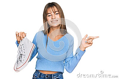 Teenager caucasian girl taking casual white shoes from box smiling happy pointing with hand and finger to the side Stock Photo