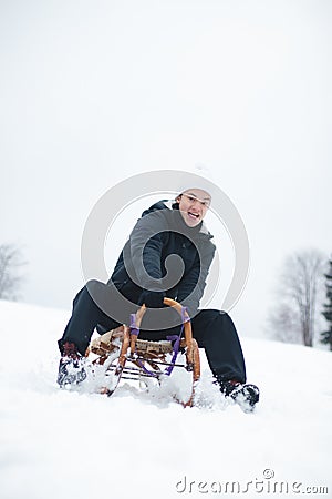 Teenager caught riding on a wooden sledge trying to adjust his direction with his hand and concentrating on his ride. In winter, Stock Photo