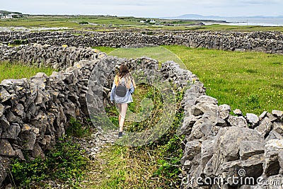 Teenager girl with backpack on a warm sunny day walking on footpath between stone fences. Inishmore, Aran Islands, County Galway, Stock Photo