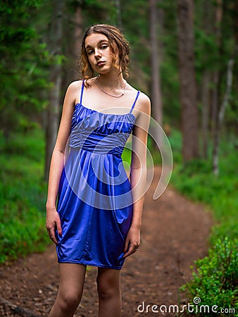 Teenager girl in a blue high fashion dress posing on a footpath in a forest. Senior prom pictures. Glamour and elegance concept. Stock Photo
