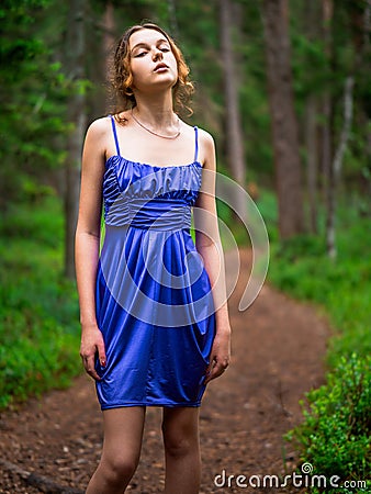 Teenager girl in a blue high fashion dress posing on a footpath in a forest. Senior prom pictures. Glamour and elegance concept. Stock Photo