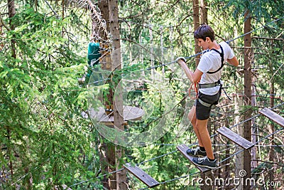 Teenager having fun on high ropes course, adventure park, climbing trees in a forest in summer Stock Photo