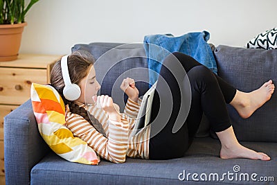 Teenager with headphones on lies on couch and listens to music. girl with tablet Stock Photo